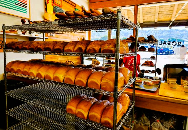 Rows of fresh hot bread loaves stacked on wire shelves in the bakery.