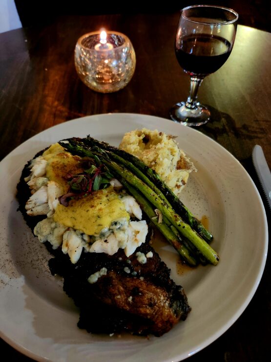 A plate filled with prime rib topped with crab, asparagus, and potatoes.