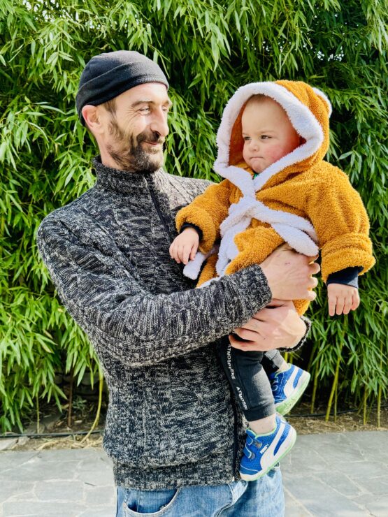 Georgian man with his son covered in a yellow coat in his arms visiting Guiaani Winery