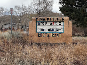 A roadside sign for Tiwa Kitchen made out of adobe, standing on scrubland