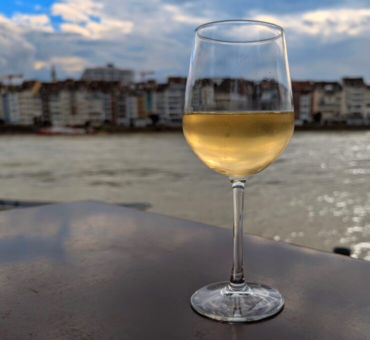 Glass of white wine on a table, with the Rhine River and downtown Basel in the background.