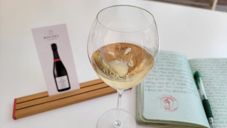 glass of Champagne next to a card for champagne tasting in Epernay and writer's notebook