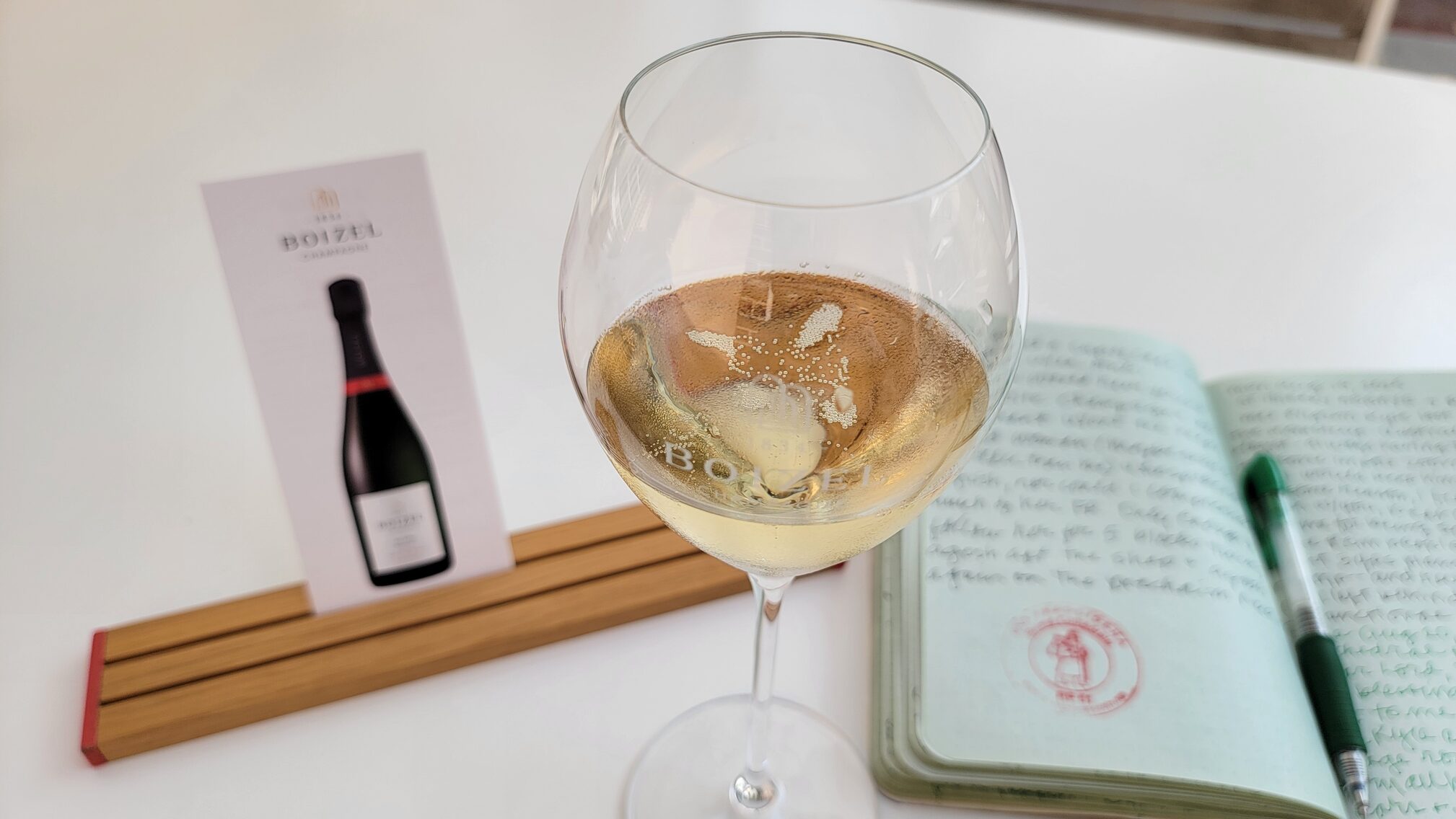 glass of Champagne next to a card for champagne tasting in Epernay and writer's notebook