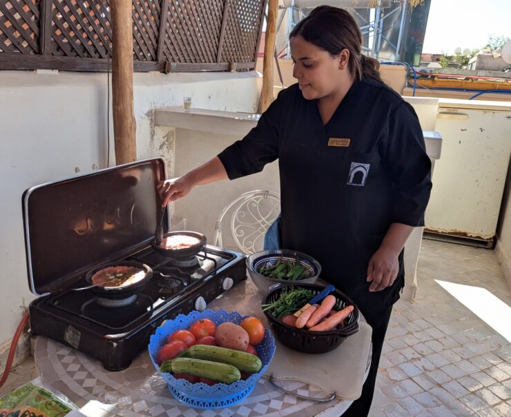 A Moroccan woman standing by a two-burner portable stove in an open air, rooftop kitchen.