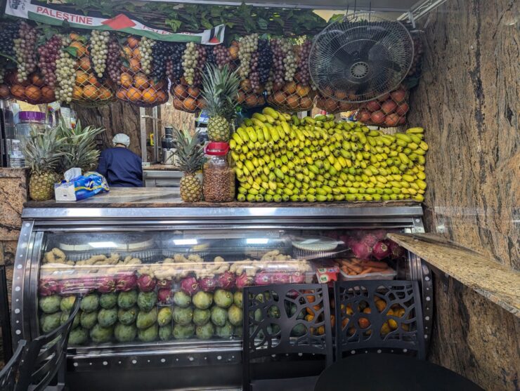 Many fruits are hanging from the ceiling in nets and displayed in and on a case.