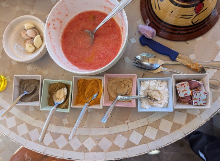 Bowl of pureed tomato and six square dishes holding spices and garlic on a table.