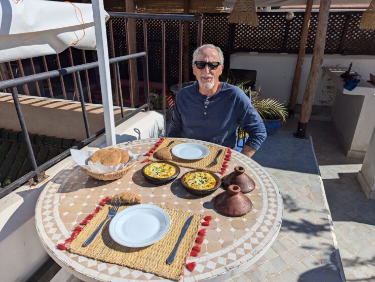 A man is seated at a table in front of the the cooked kefta tagine and a basket of bread. 