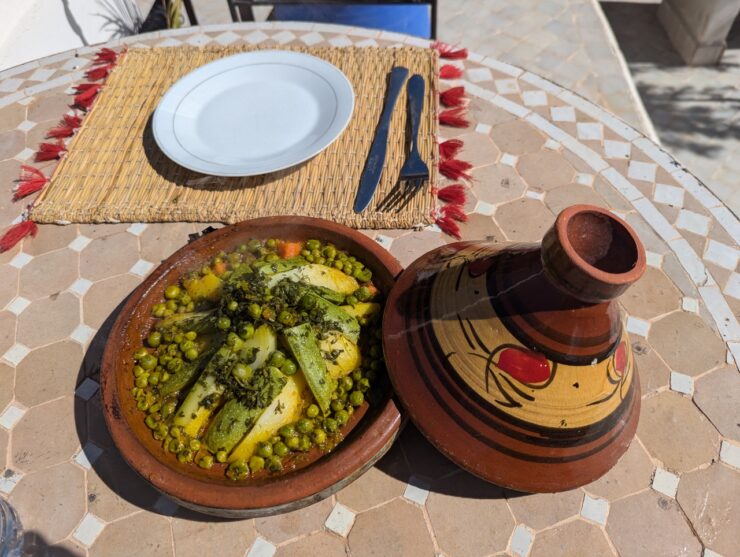 A cooked vegeable tagine is placed on a table with the cone shaped lid to the side.