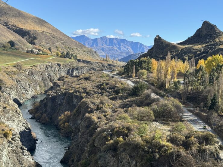 Landscape of deep gorge with river on left and hill with trees on white with mountains in background