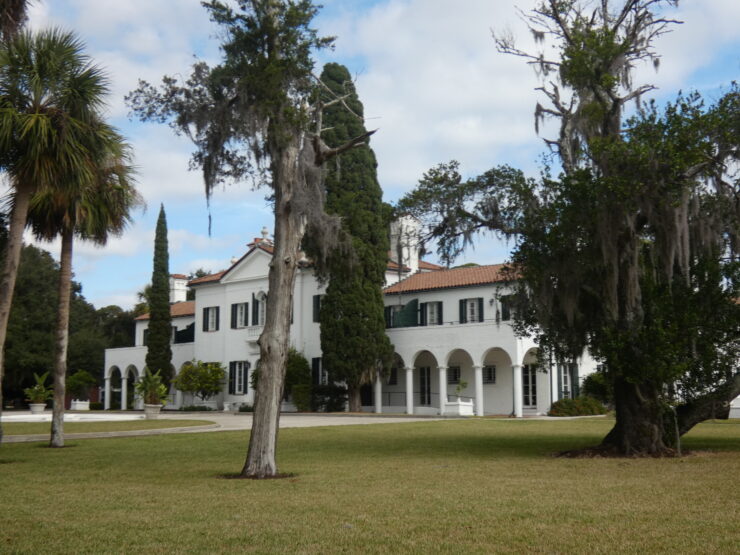 Large white mansion with lawn and trees in front.