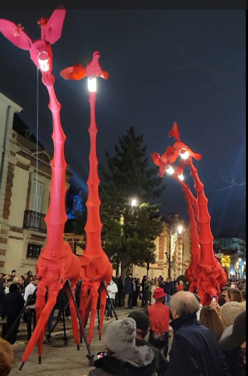 tall red giraffes walk down Ave de Champagne during one of the Habits de Lumière Epernay parades