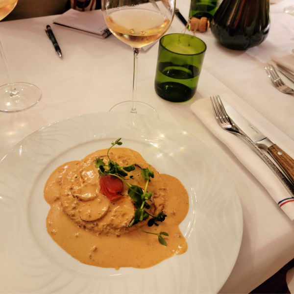 sliced white sausage covered in golden cream sauce with glass of Champagne on linen tablecloth