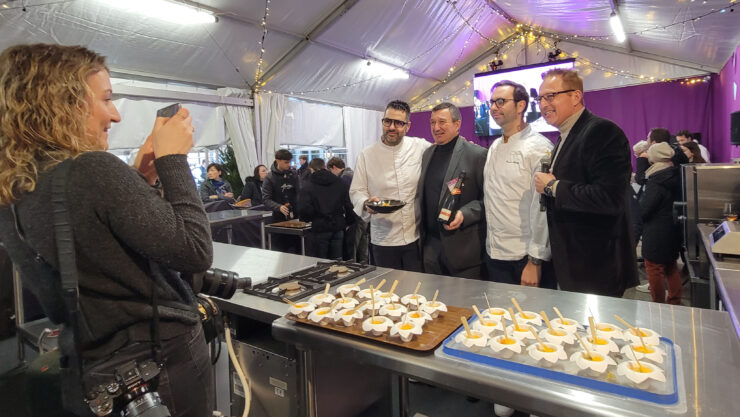 woman journalist snaps photo of 4 men under the Habits de Saveurs white tent decorated with lights