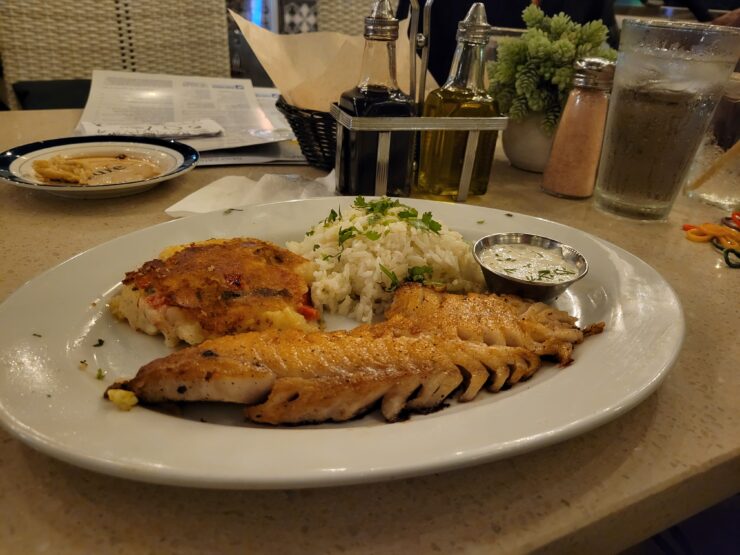 White dinner plate with grilled rockfish, rice, and fried potato cheese cake at Lure Fish House.