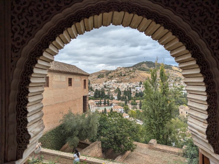 View of a hillside dotted with houses viewed through an arched palace window at the Alhambra