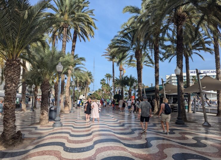 Wavy tile pattern with alternating black, beige and pink tile creates visual interest on the esplanade. Palm trees frame the walkway. 