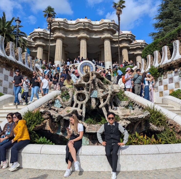 A building with many curves and 5 columns with an outdoor dual staircase on either side packed with tourists