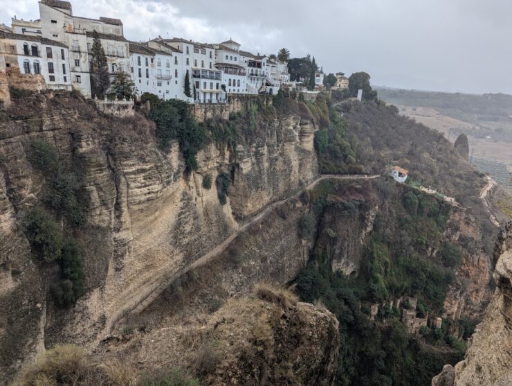 A deep gorge with sheer cliff face is topped with four story buildings built side by side with no space between them. 