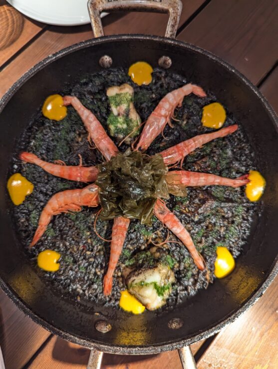 Large cast iron skillet holding black rice and an artistic display of prawns in a star shape