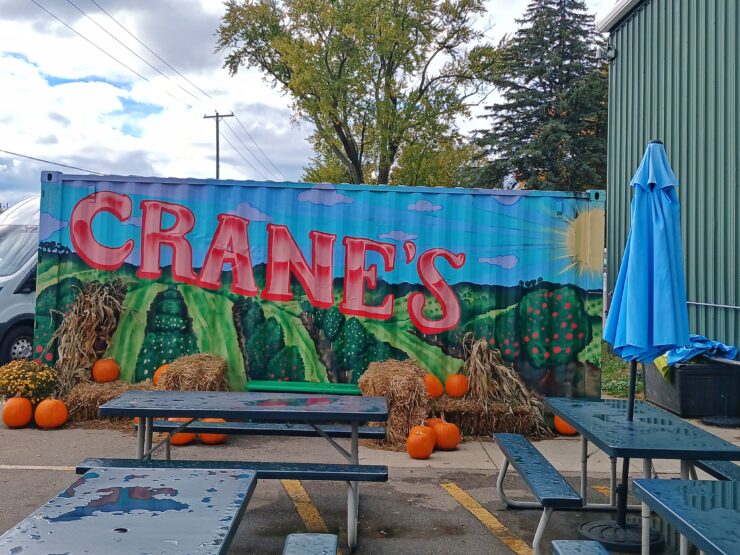Metal shipping container painted with an orchard scene and the name Crane's