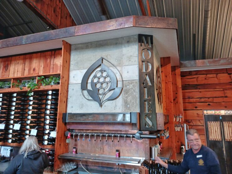 Warm wooden interior of Modales winery, wine bottles displayed on the back wall with workers pouring wine in front