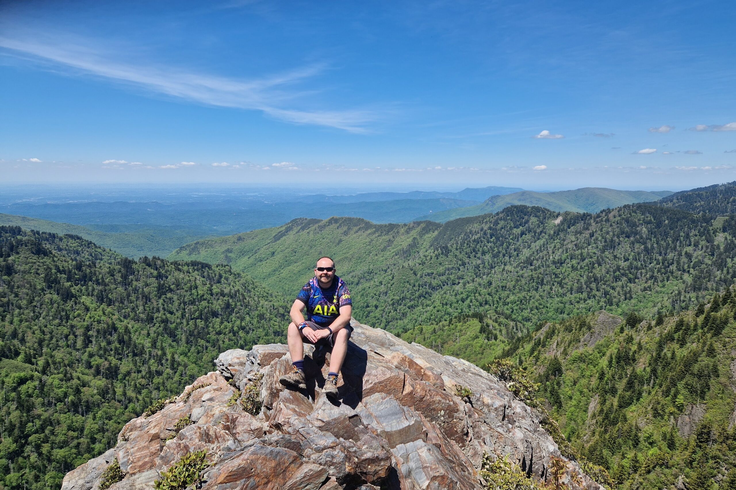 Man sitting on rocky outcrop with backdrop of forest and blue sky