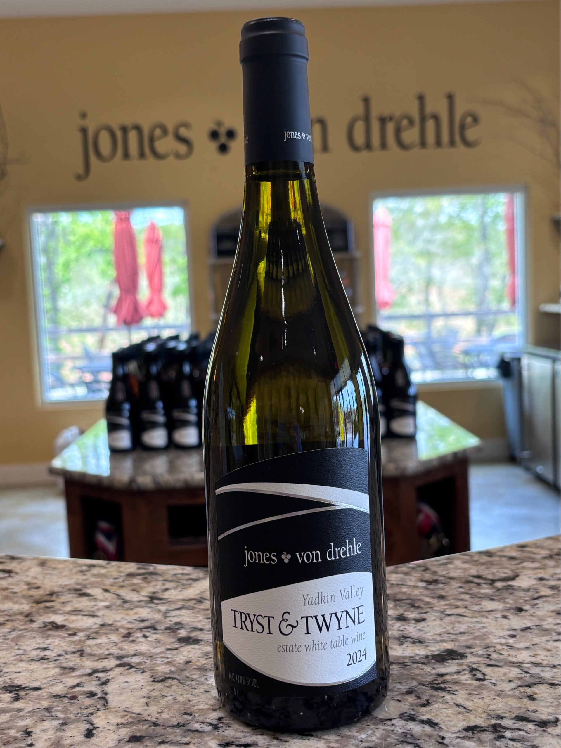 A bottle of wine stands on a marble counter in front of a dozen other bottles