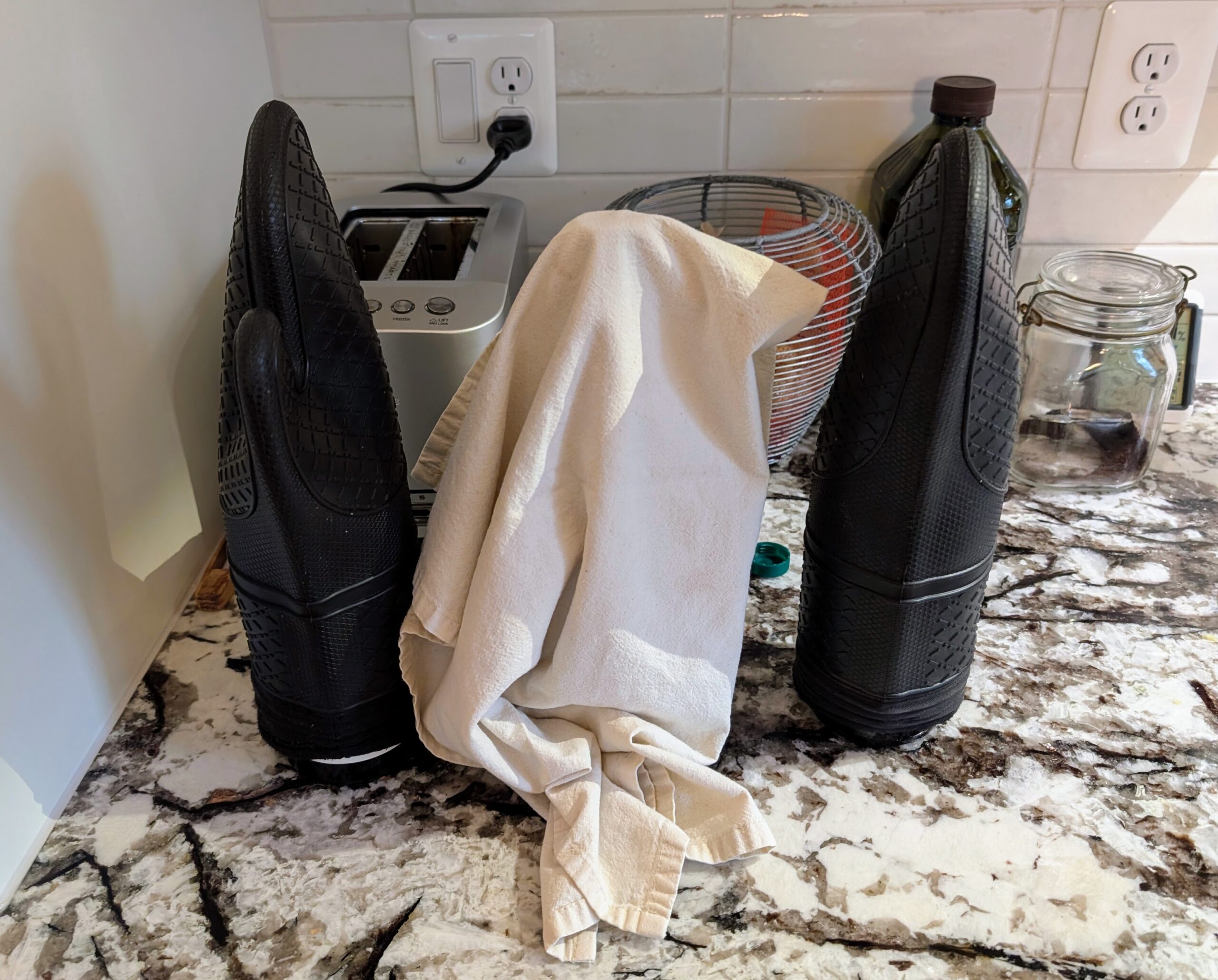 two kitchen mitts and one kitchen towel covering wine bottles