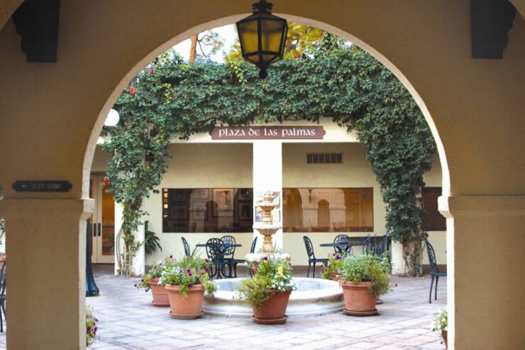 Arched walkway opening into a candlelit courtyard at Mission Resort + Club, with potted plants, greenery, and Mediterranean-style architecture.
