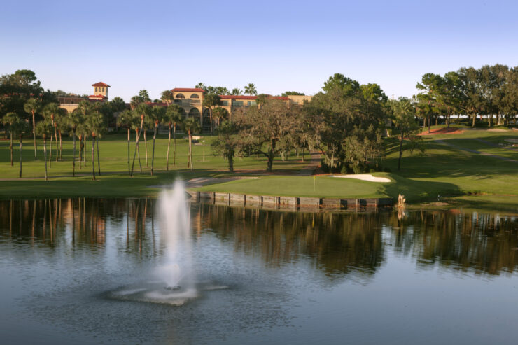 El Campeón golf course at Mission Resort + Club with a calm pond, sand bunkers, rolling fairways, and resort buildings in the distance.