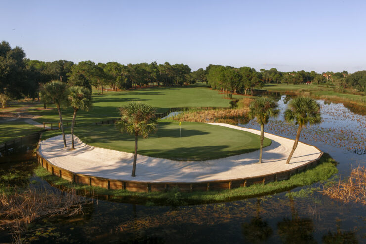 A scenic green on El Campeón golf course at Mission Resort + Club, surrounded by water, sand bunkers, and lush Central Florida landscaping.