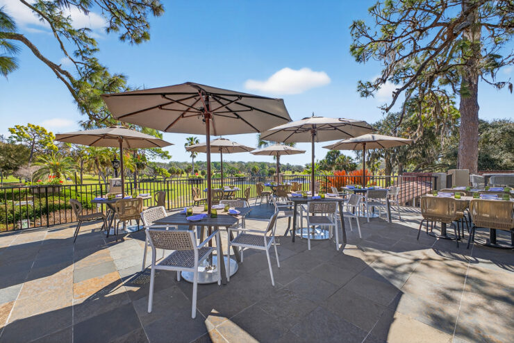Outdoor dining patio at Conquistador Restaurant at Mission Resort + Club, with tables, chairs, umbrellas, and resort landscaping.