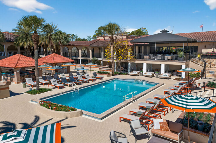 Outdoor swimming pool at Mission Resort + Club with lounge chairs, umbrellas, palm trees, and resort buildings under a bright blue sky.