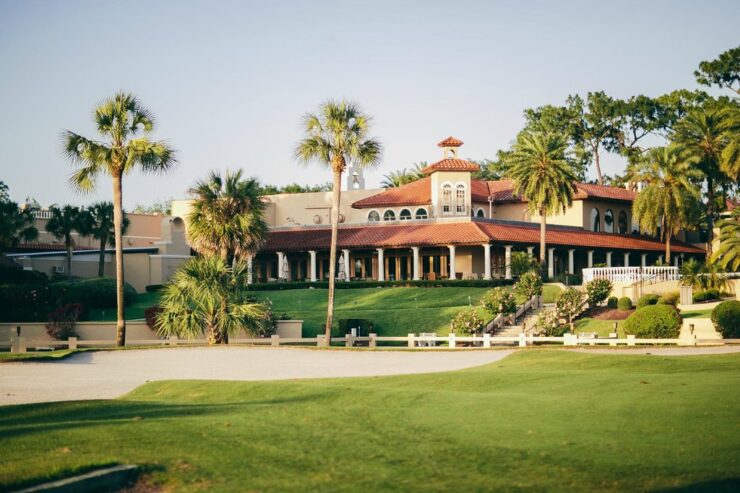 The Mission Resort + Club viewed from the golf course, with palm trees, manicured grounds, a sand bunker, and Mediterranean-style resort architecture.
