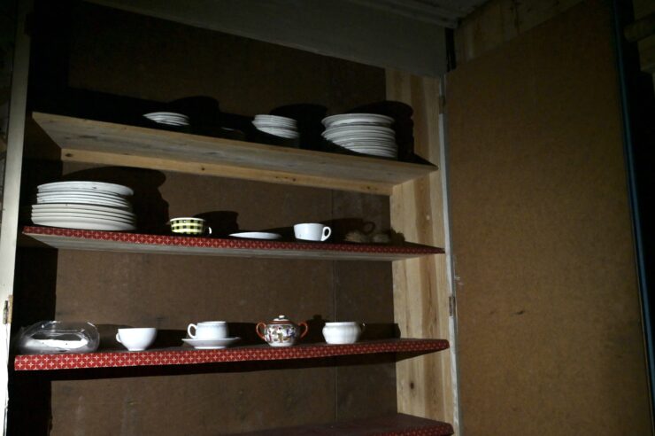 Dishes line the shelves in the dark interior of and abandoned building.