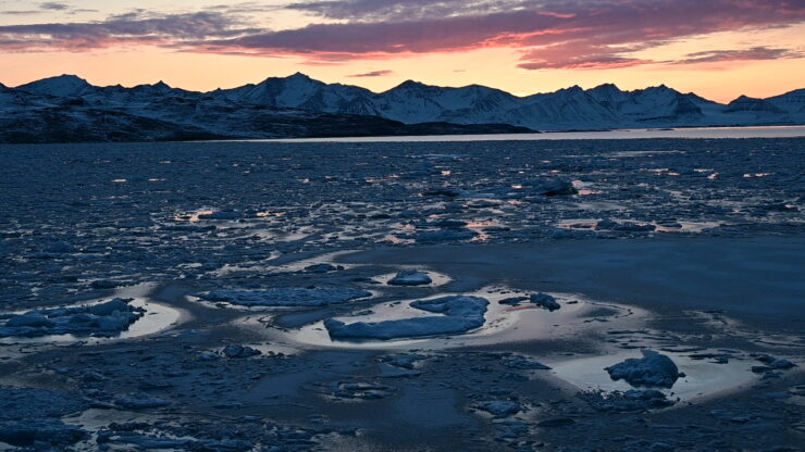 The sun sets over floating ice and behind the mountains of a fjord in Svalbard.