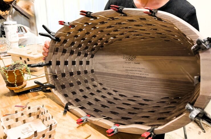 The image shows a handcrafted wooden basket with the verse written inside the basket.