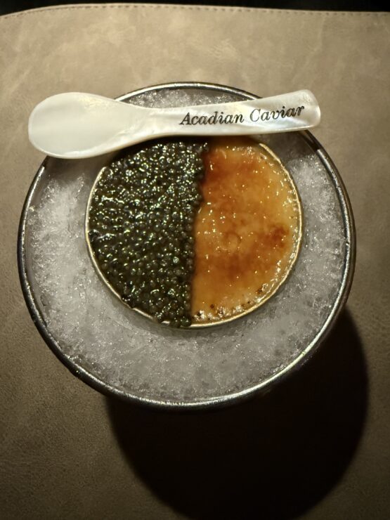 An image of a caviar spoon with caviar and caramel in round dish.