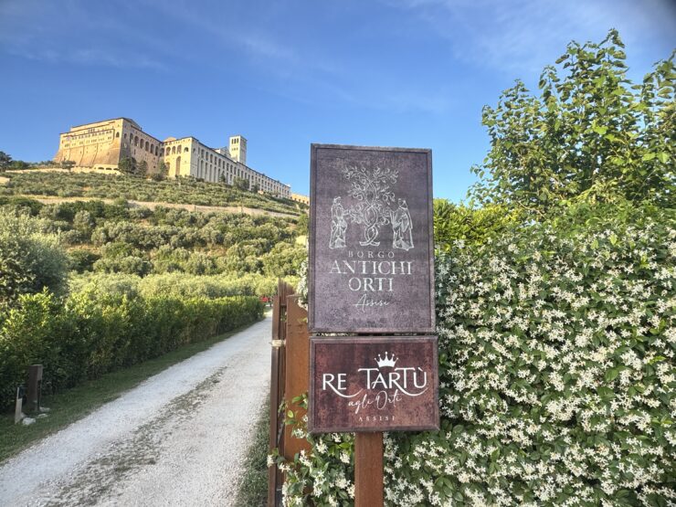 Roadsign reading Borgo Antichi Orti besides a grey road with a basilica on the hill behind