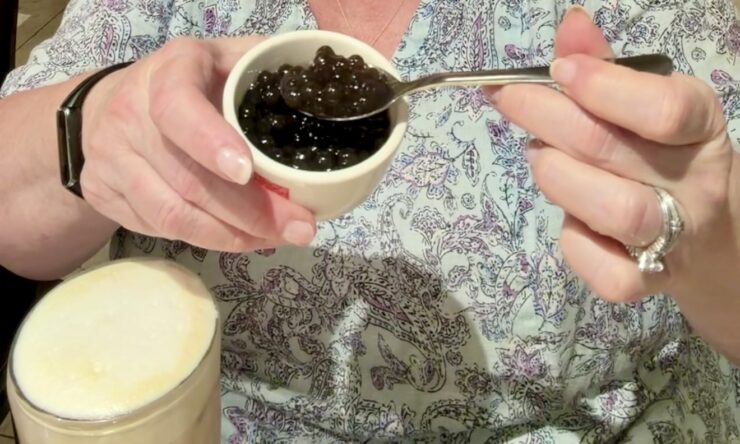 Women has a glass of iced milk tea and adds tapioca pearls to create bubble tea