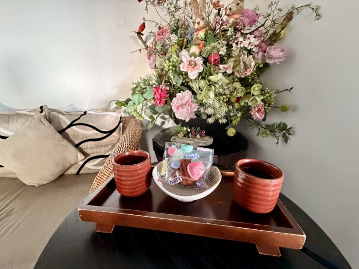 Two tea cups and a snack on a tray in front of a bouquet of flowers.
