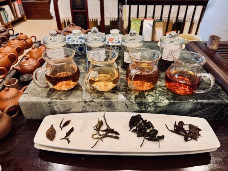 Tea leaves on a plate in align with small pitchers of tea brewed from the leaves.