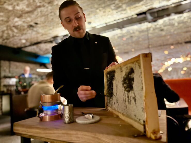 A server removes honey from a comb in a wooden frame to prepare a sauce tableside at Tanière³