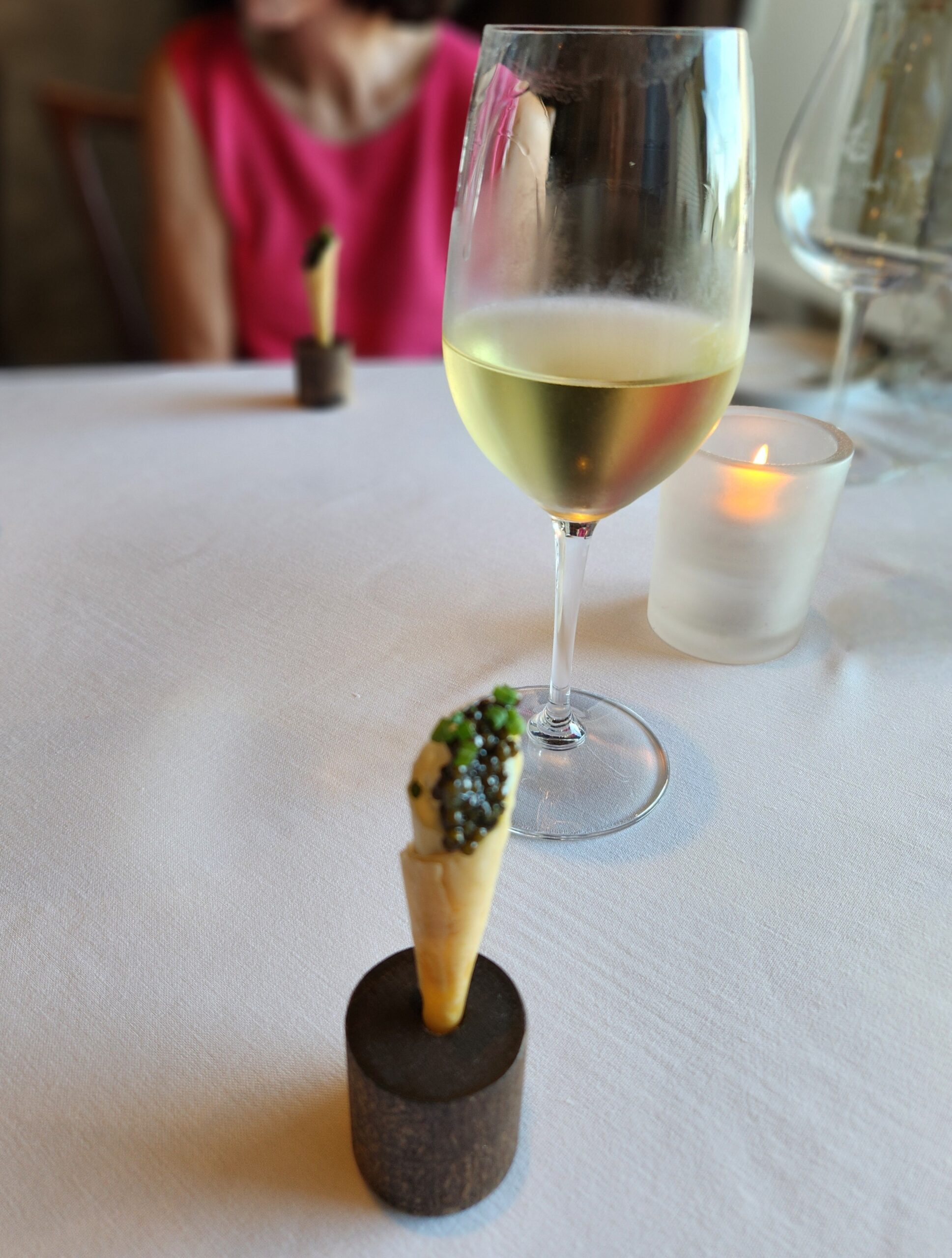A cone of phyllo dough, filled with truffle cream and topped with caviar standing upright in a small round stand.