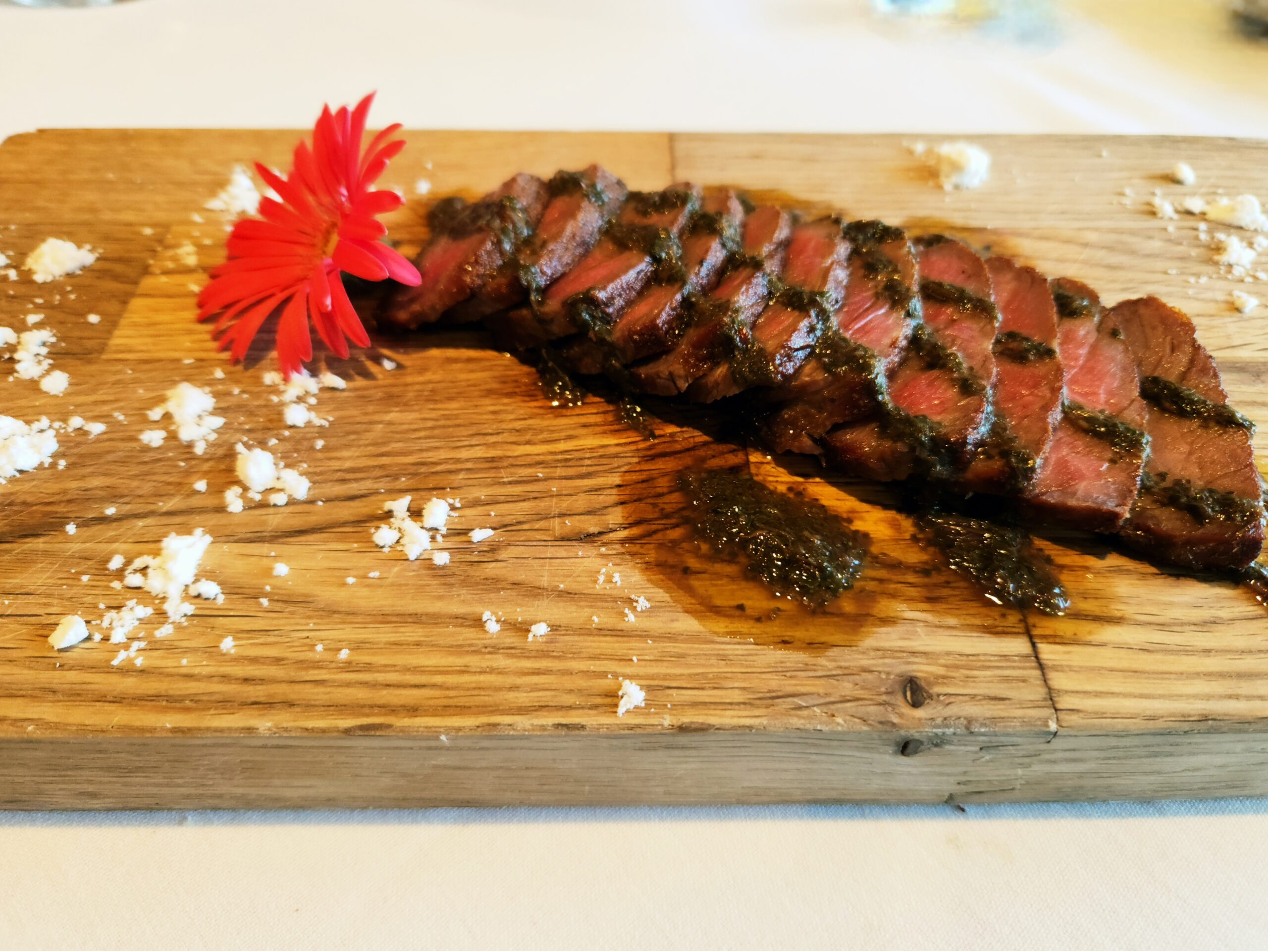 A steak, sliced and fanned out on a serving board, topped with an edible flower and shaved white truffles.