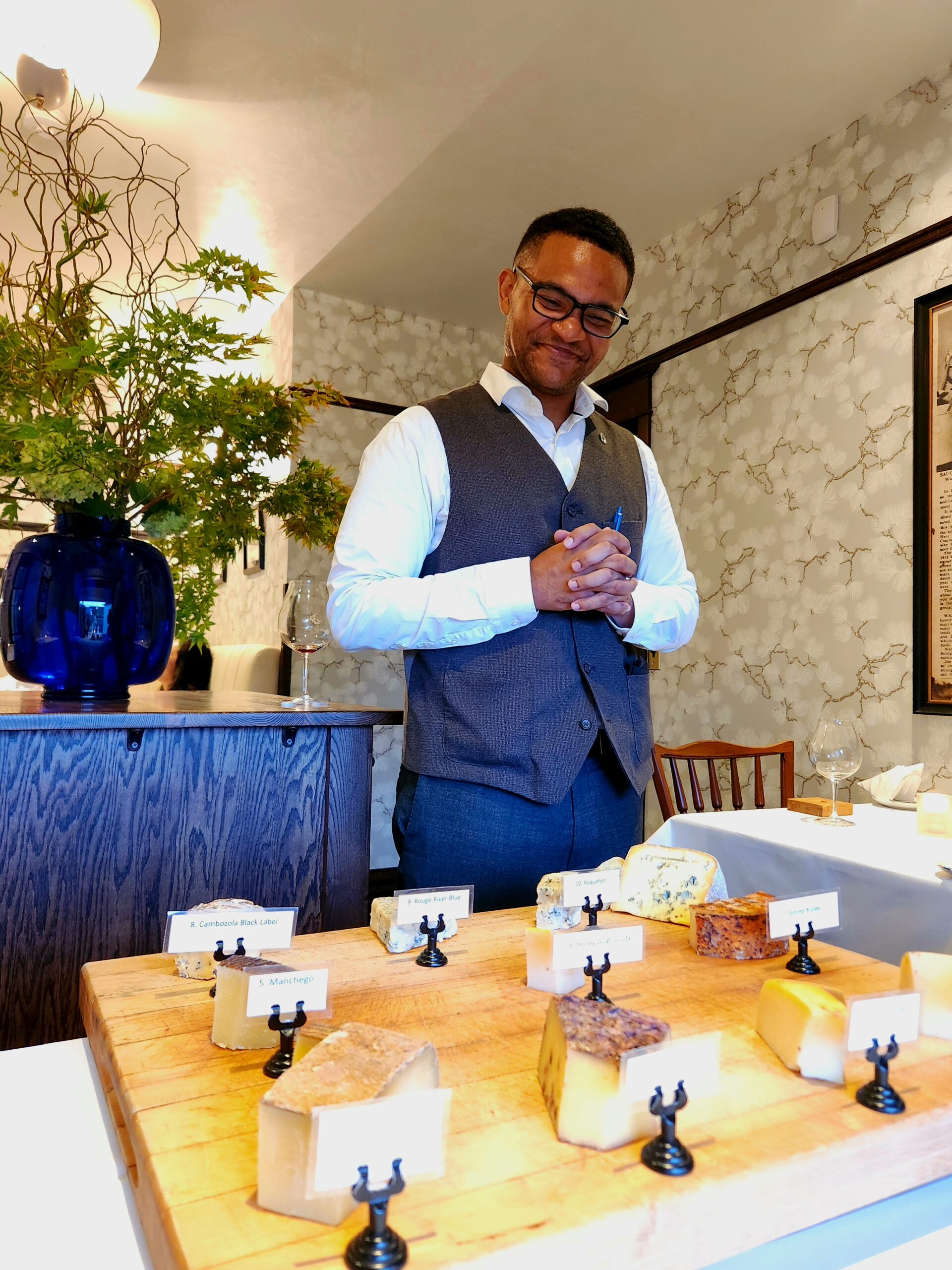 A smiling server stands ready to introduce guests to a plethora of cheeses on his mobile cheese board.