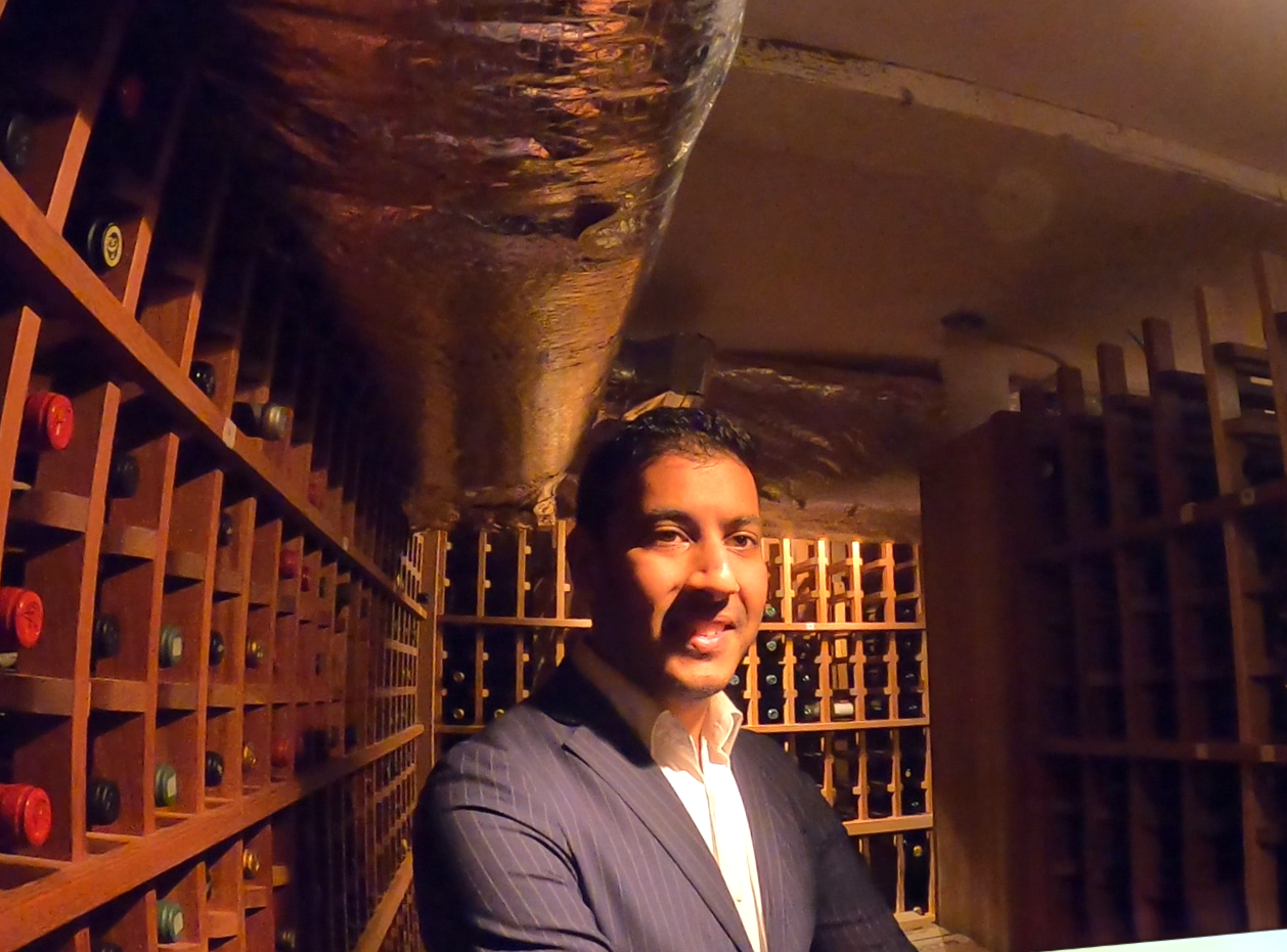 A man standing in the wine cellar, surrounded by wine bottles.
