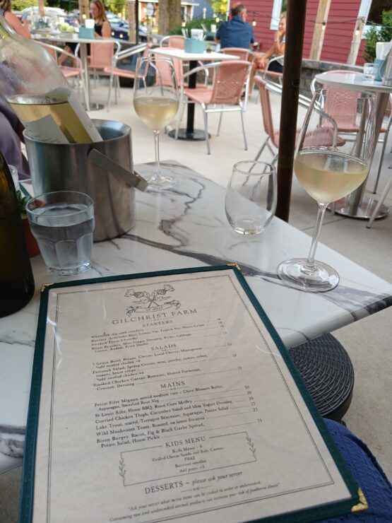Table holding ice bucket with wine bottle, two glasses of white wine, and menu