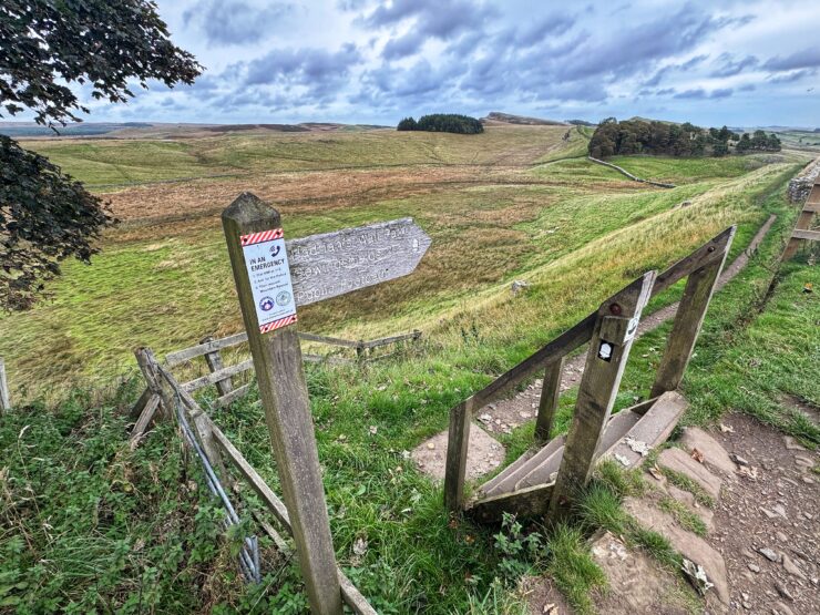 A sign reading Hadrian's Wall against a countryside backdrop of green hills